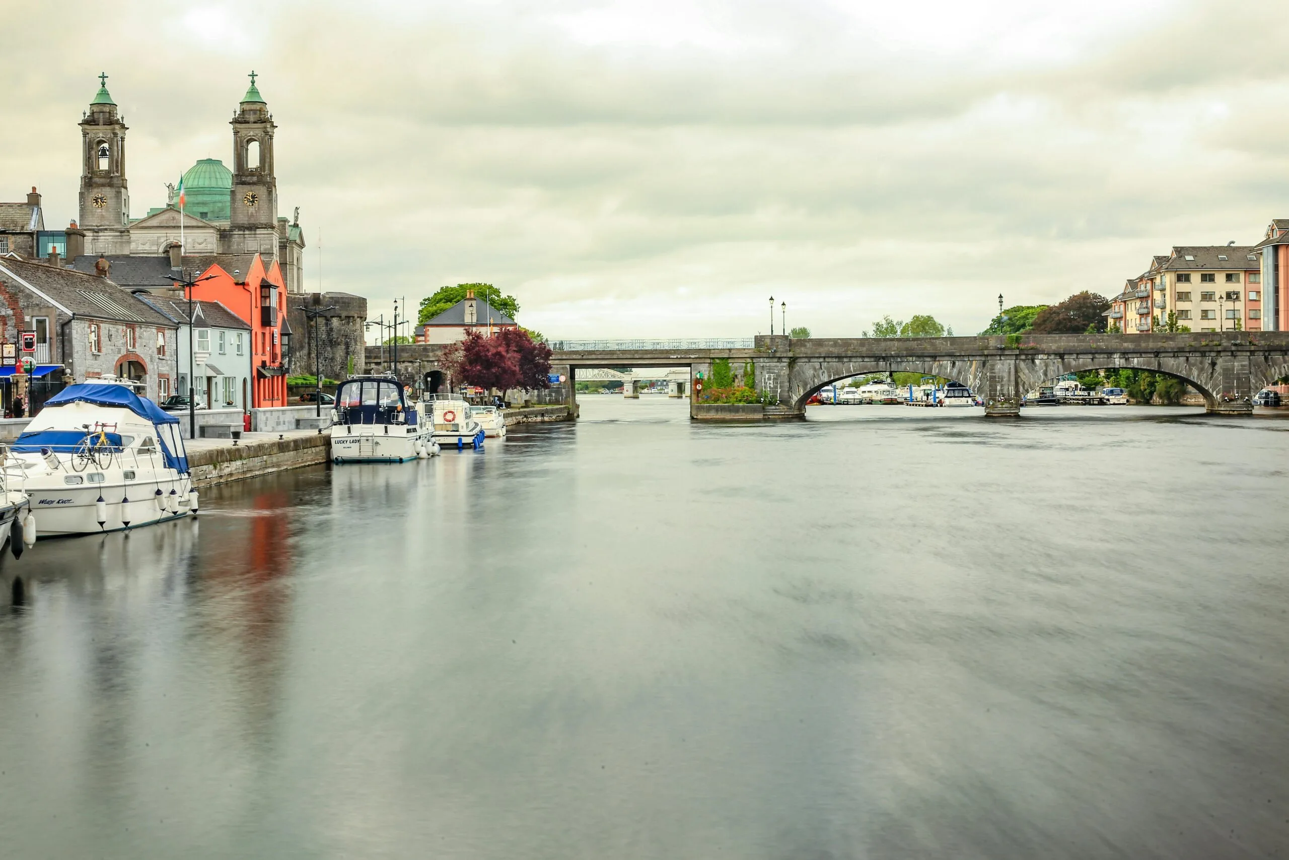 Picturesque scene of Athlone bridge over a calm river in Ireland with boats and historic buildings.